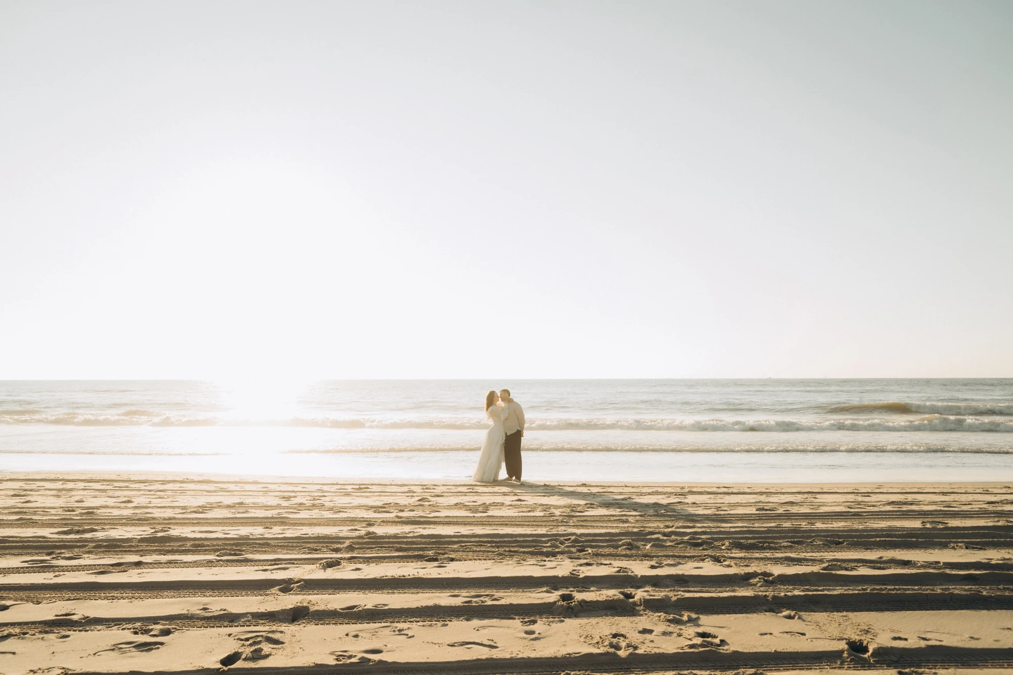 Couple on a wide sunlit beach with the sea behind them