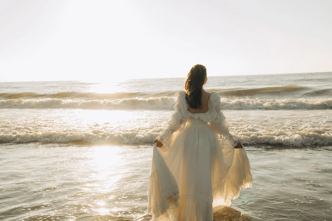 A woman in a flowing white dress facing the sea