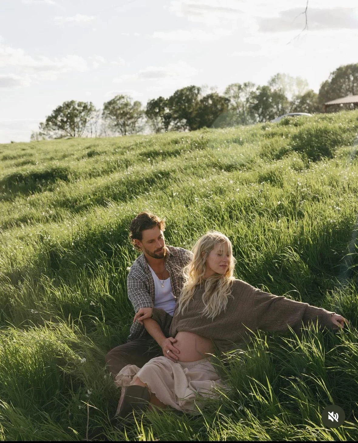 Expectant parents standing close together in a green field