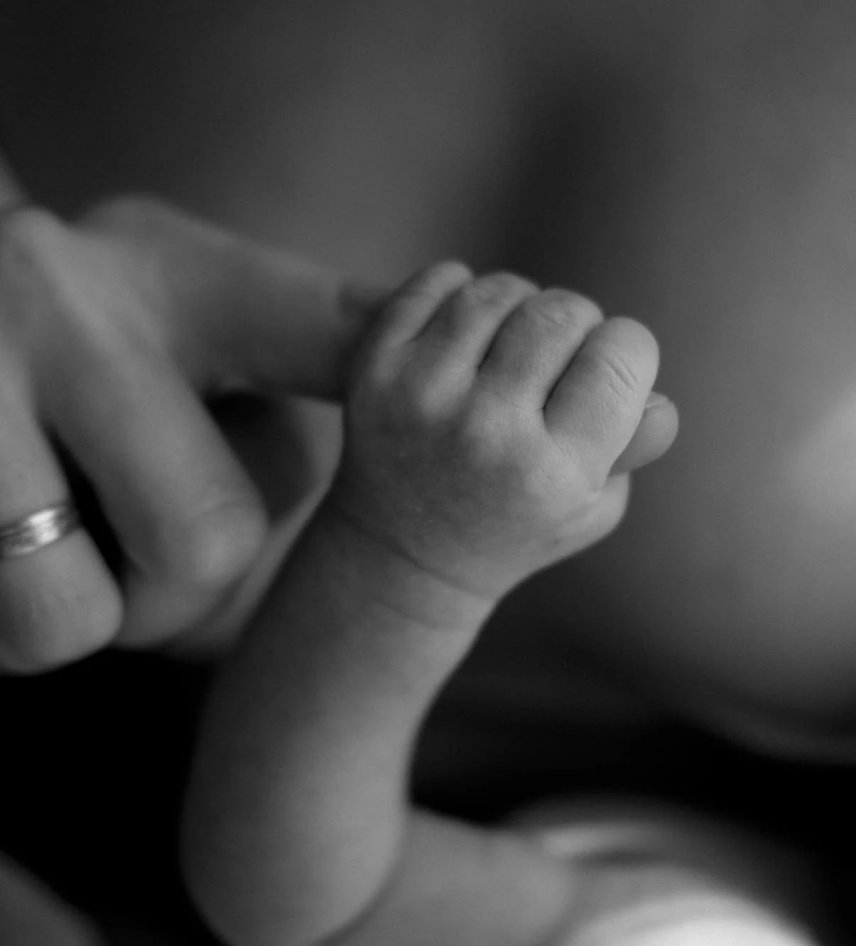 Baby holding a parent’s finger, photographed in black and white
