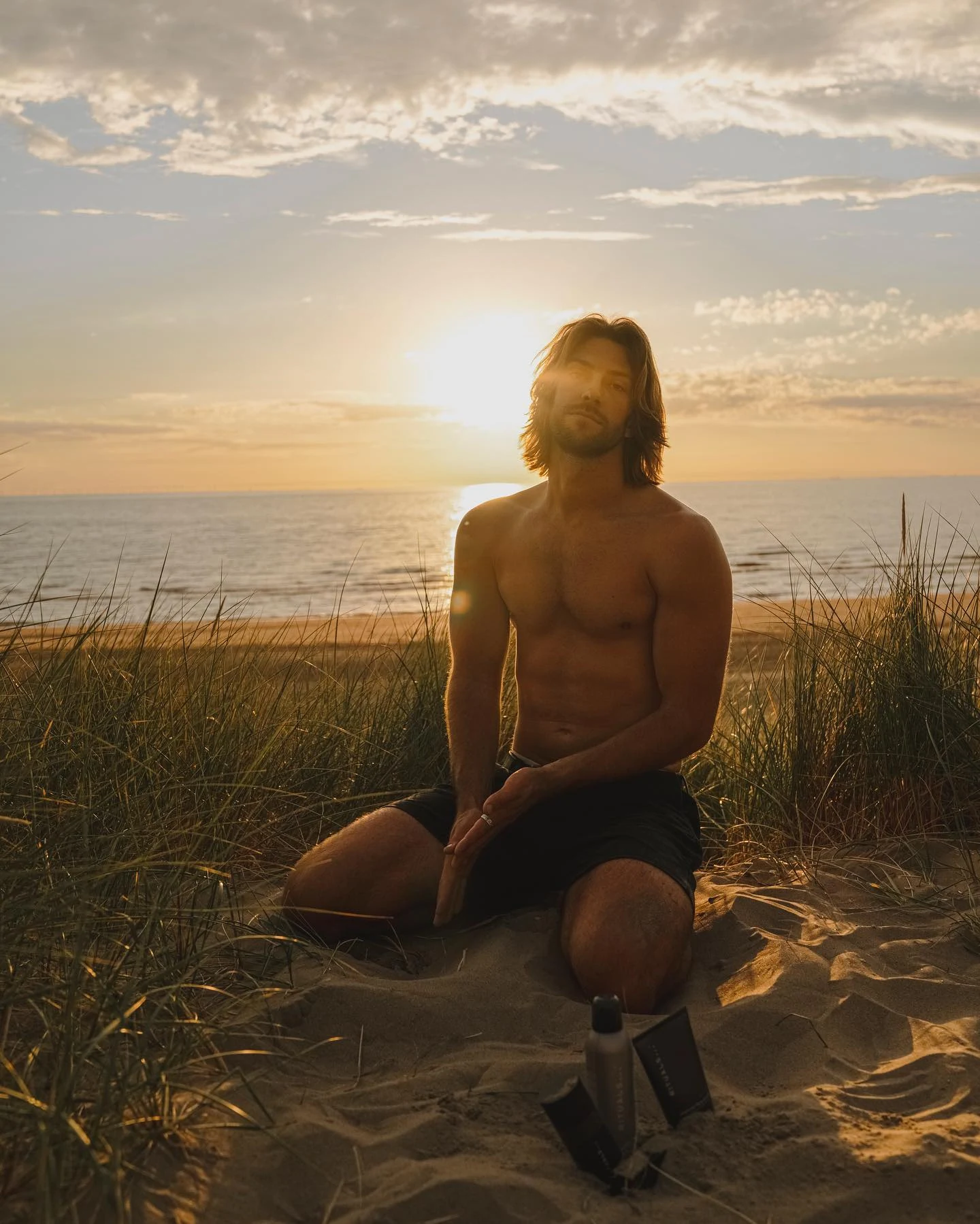Man seated in dune grass under a glowing sunset