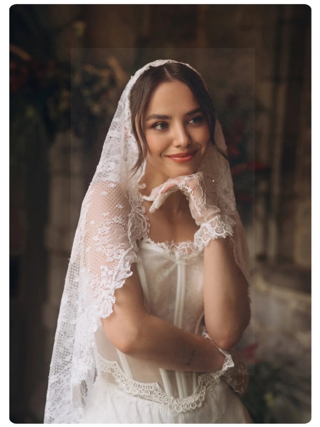 Bride looking over her shoulder in a lace veil, lit by a window