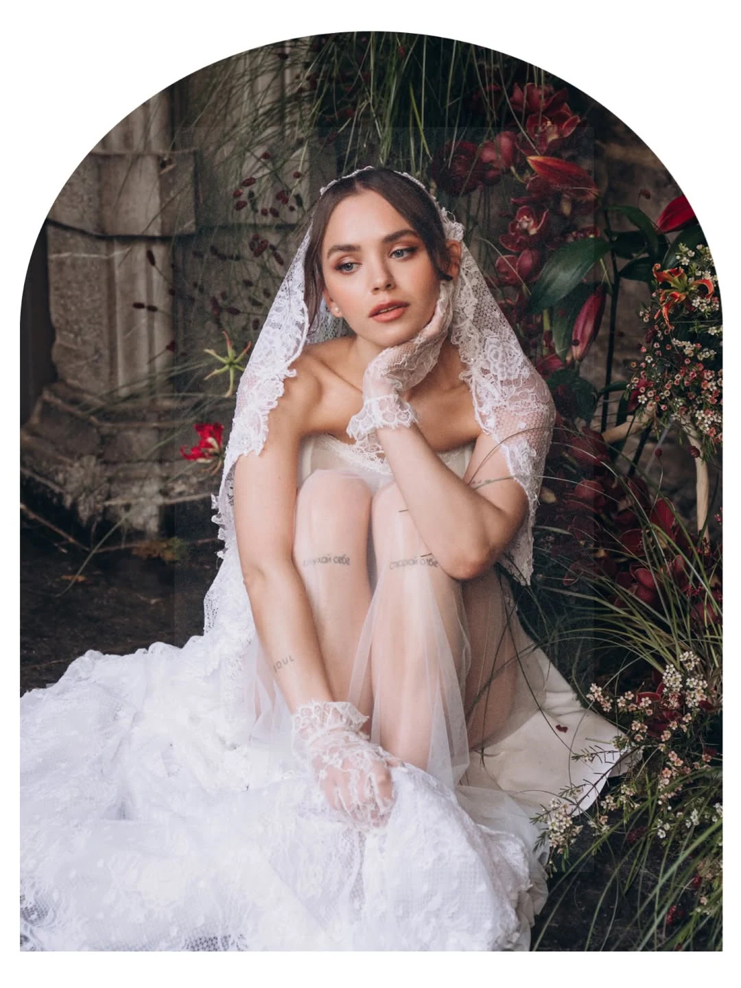 Bride seated beside flowers in an arched photographic composition